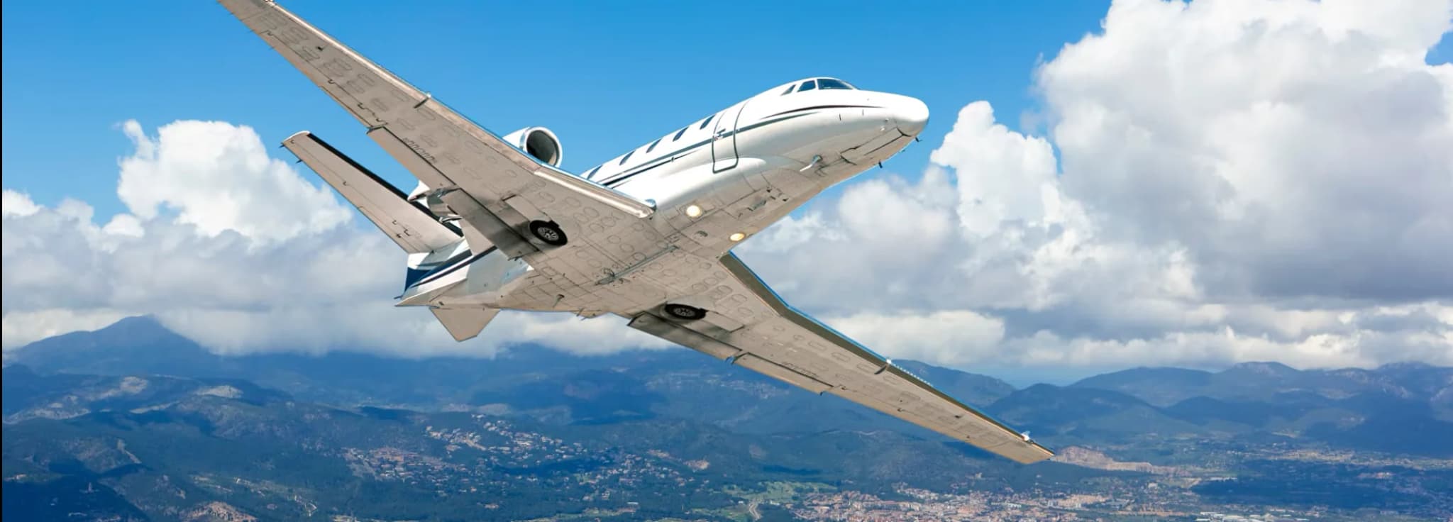 Private business jet flying low over a scenic coastal city harbor and mountain background.