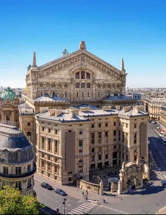 High-angle daytime view of the historic Palais Garnier opera house surrounded by traditional Haussmann architecture and Parisian rooftops.