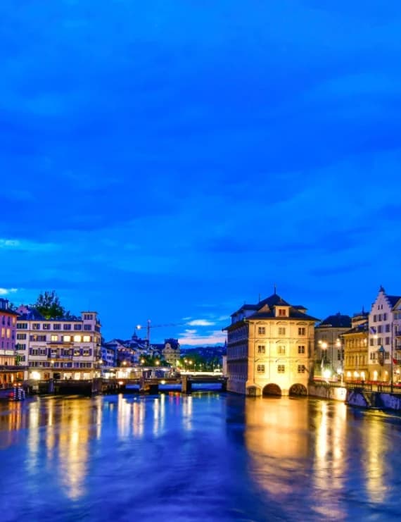 Panoramic twilight skyline view of Zurich showing the Limmat River, Fraumünster, and Grossmünster.
