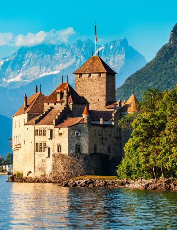 The medieval Chillon Castle sitting on a rocky islet along the shore of Lake Geneva with snow-capped Alpine mountains in the background.