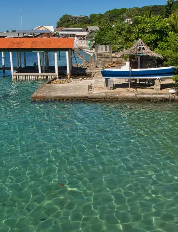 Crystal clear turquoise Caribbean water reflecting light next to a wooden boat dock and tropical coastline in Honduras.