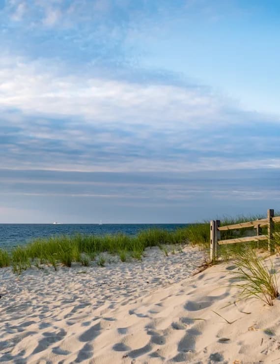 Sandy beach dunes with beach grass and a wooden split-rail fence overlooking the ocean in Nantucket