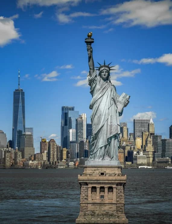 Front view of the Statue of Liberty on Liberty Island with One World Trade Center and Manhattan skyscrapers under a blue sky