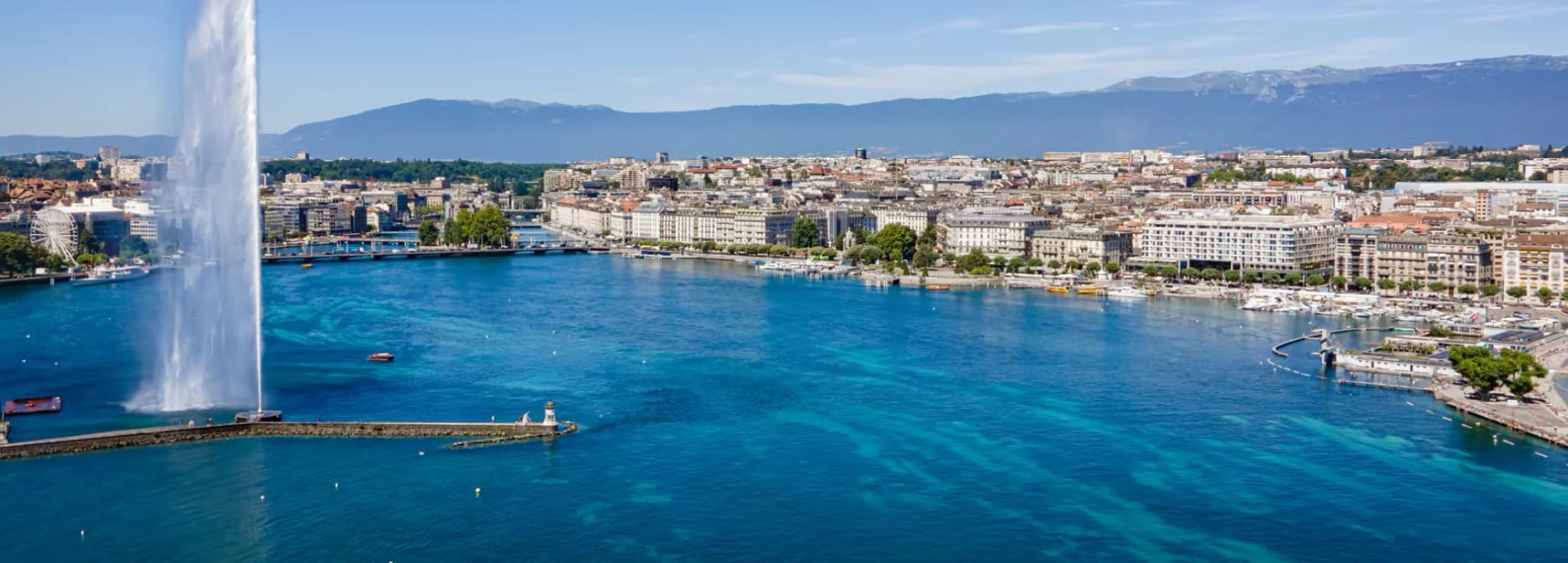 The iconic Jet d'Eau water fountain shooting high into the air on Lake Geneva with the city skyline and mountain backdrop in Switzerland.
