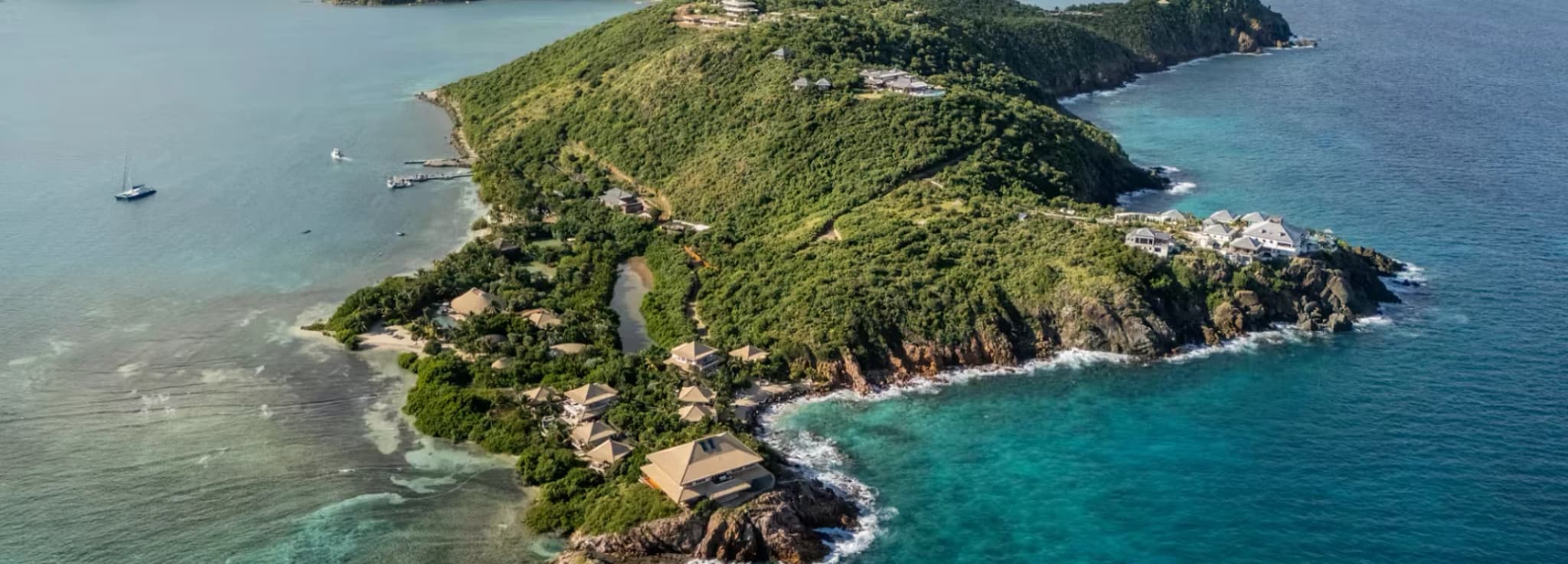 High-angle aerial panorama of the rocky coastline, turquoise reefs, and luxury estates of Moskito Island.
