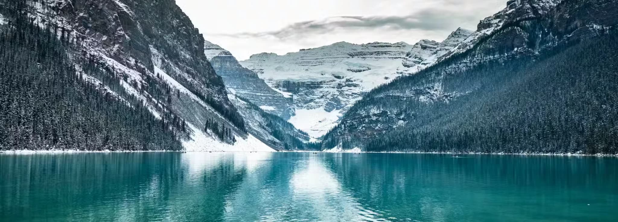 Rocky shoreline of Lake Louise reflecting the dramatic snow-capped peaks and the Victoria Glacier.