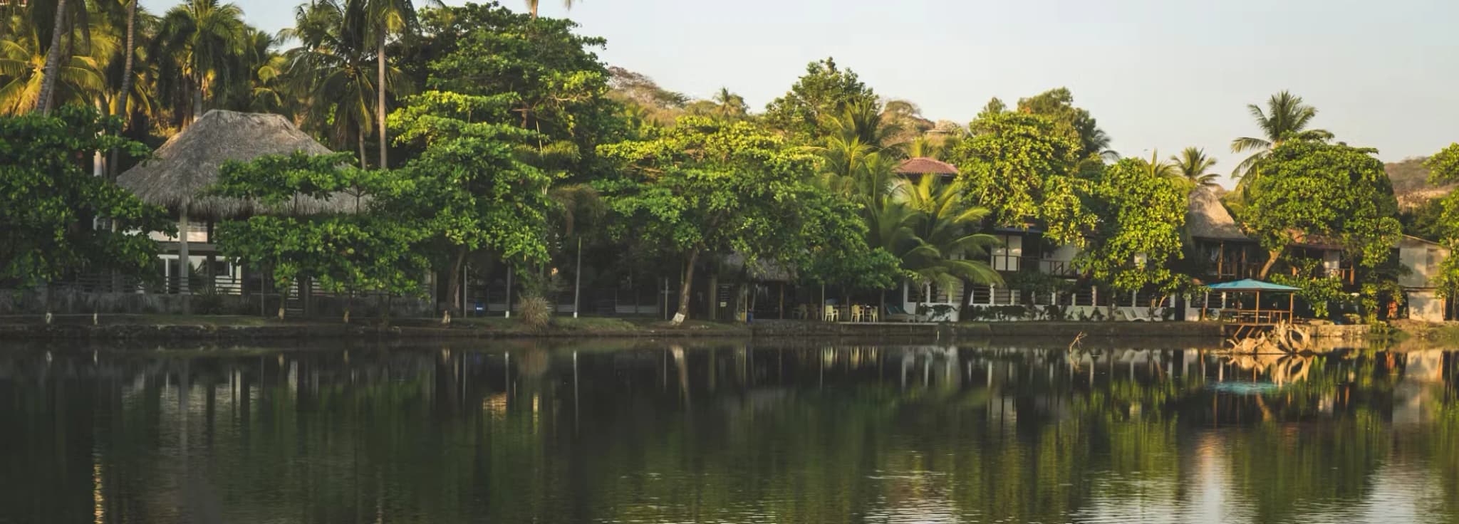 Lush tropical trees and coastal lodges reflecting calmly in the water near El Tunco beach in El Salvador.