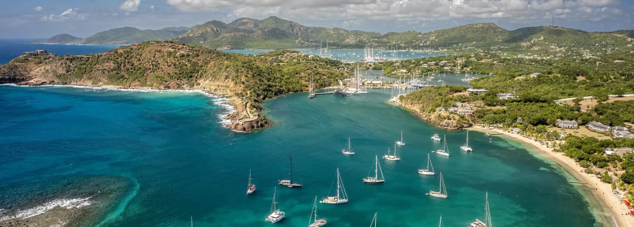 High-angle aerial drone view of turquoise blue sea, white sand beach, and anchored yachts in Antigua.