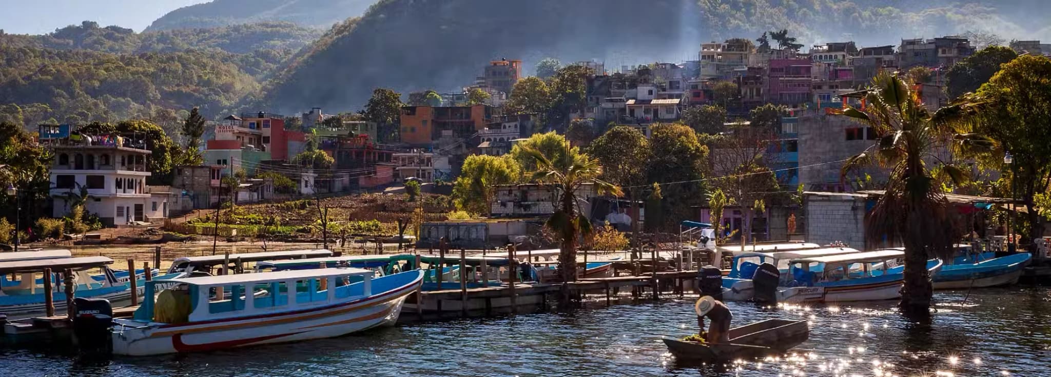 Water taxis and wooden docks on Lake Atitlan with San Pedro volcano looming in the background under clear blue skies.