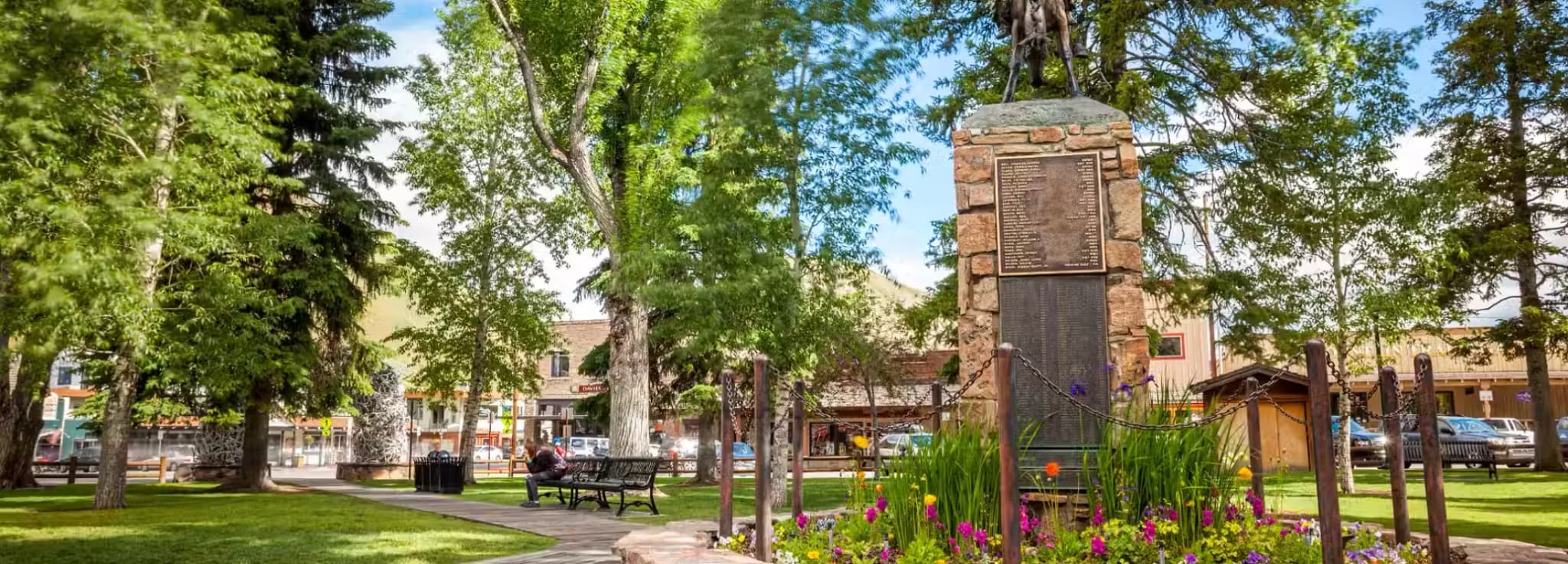 Cowboy bronze statue and stone memorial monument surrounded by flowers at George Washington Memorial Park in Jackson Hole