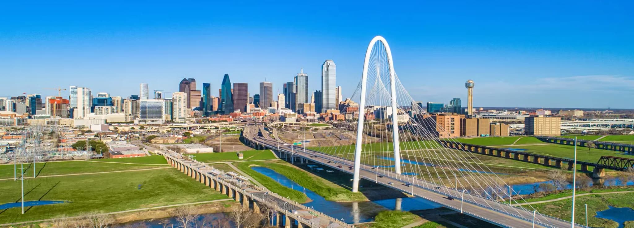 Aerial view of the Margaret Hunt Hill Bridge spanning the Trinity River with the Dallas skyline in the background.