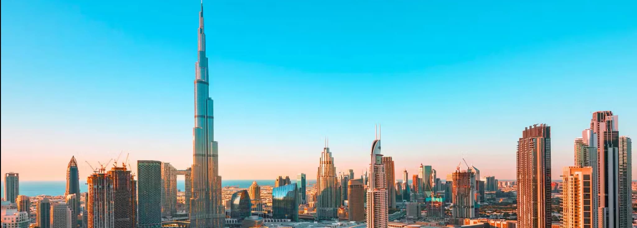Panoramic aerial view of Downtown Dubai featuring the Burj Khalifa, Dubai Mall, and surrounding skyscrapers during golden hour.