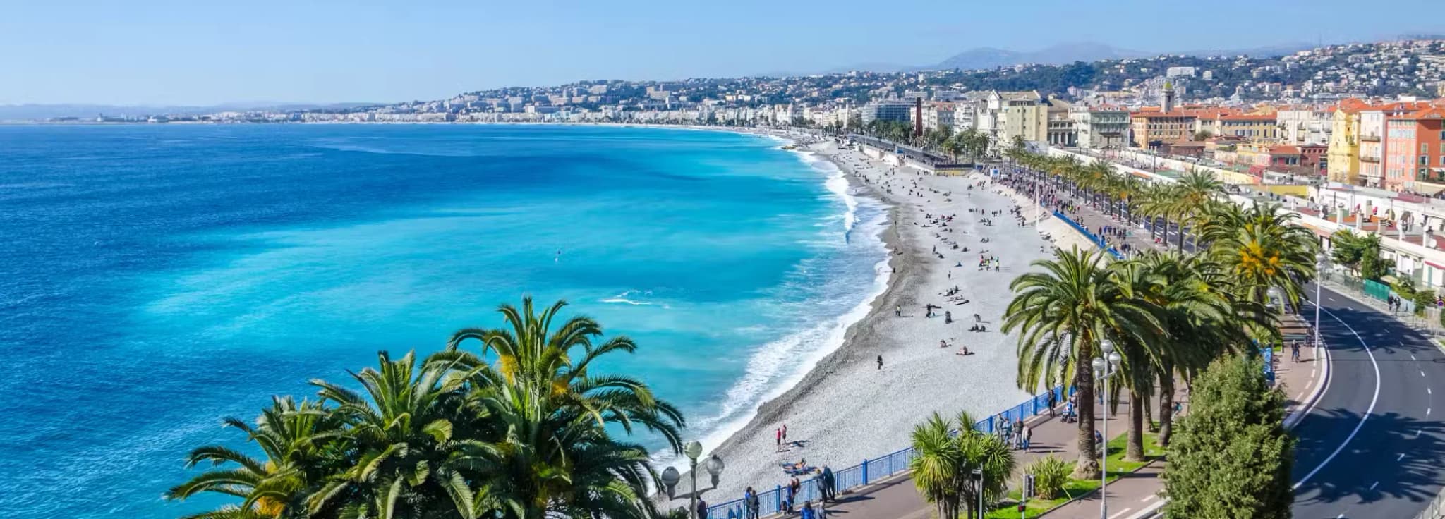 Aerial view of the turquoise Mediterranean sea and palm trees along the Promenade des Anglais beach in Nice, France.