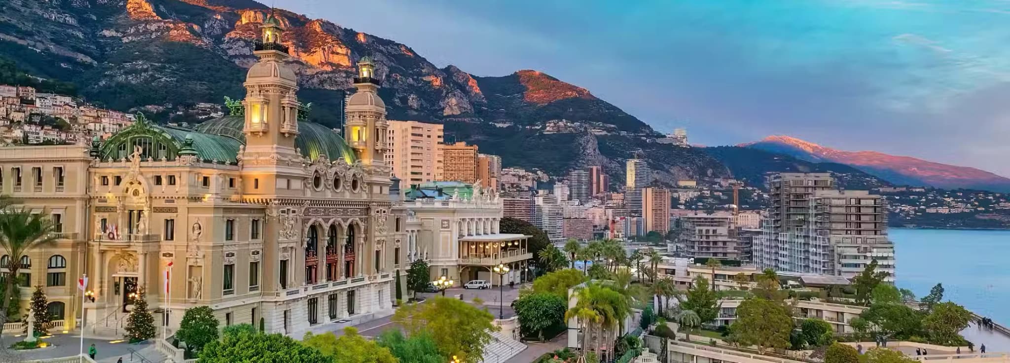 Daytime view of the ornate Monte Carlo Opera House architecture with the dramatic mountain and coastal backdrop in Monaco.