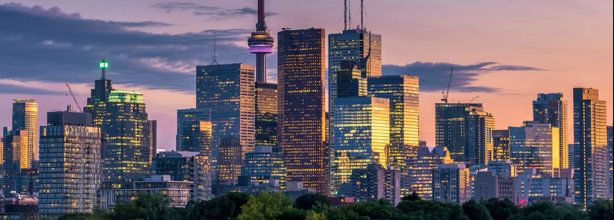 Panoramic view of the downtown Toronto skyline and CN Tower illuminated during a vibrant sunset in Ontario, Canada.