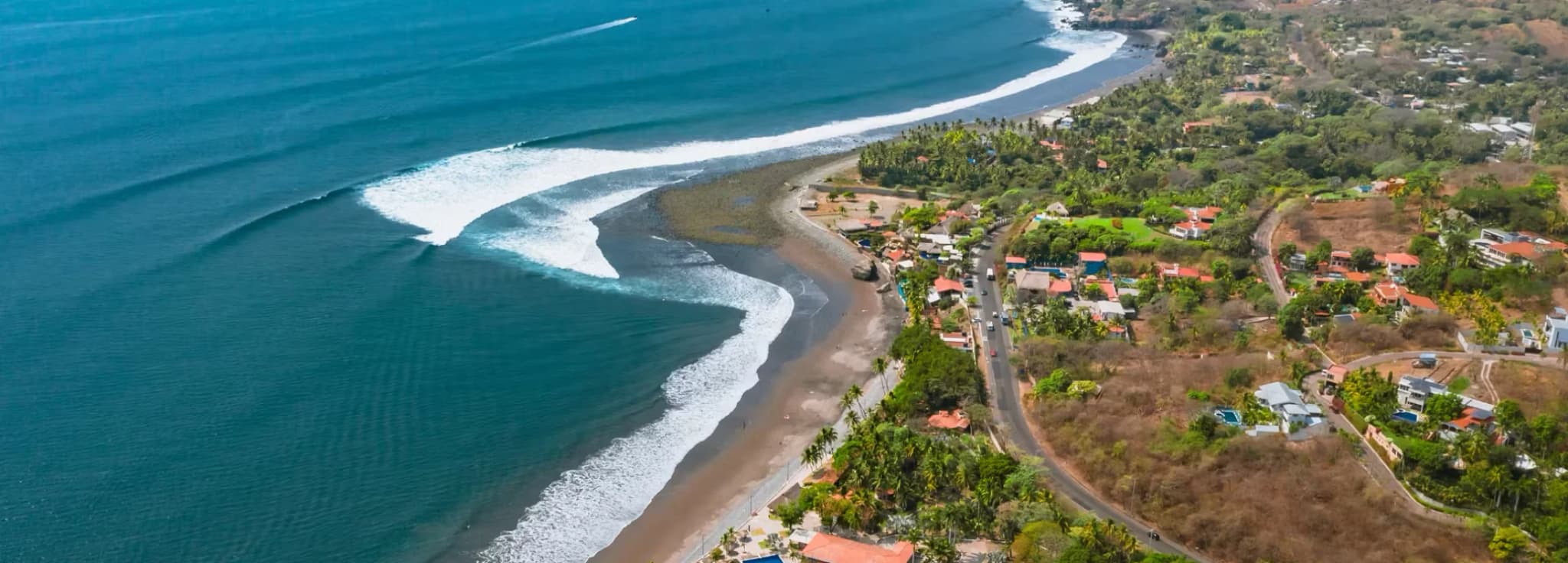 Aerial drone view of the coastline, ocean waves, and tropical resort town at El Zonte beach in El Salvador.