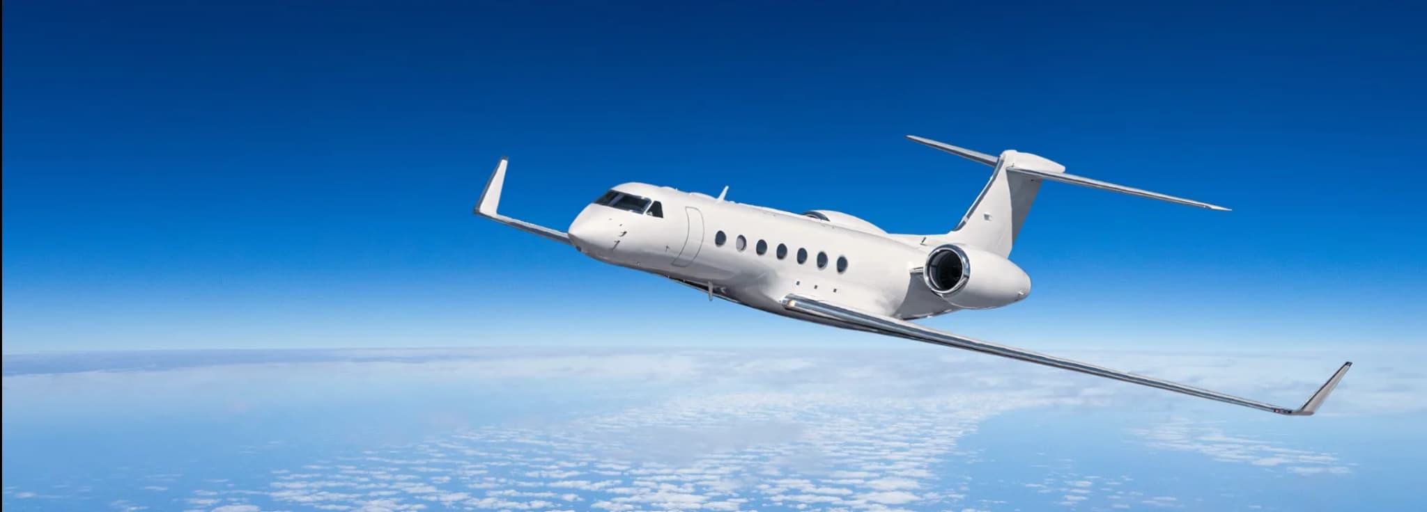 Sleek white private jet cruising smoothly at high altitude above a blanket of clouds.