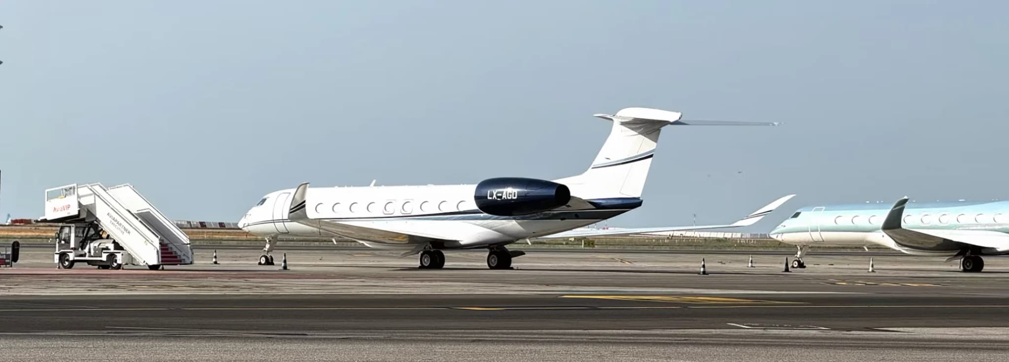 Private business jets parked on an airport apron during the day with boarding stairs nearby.