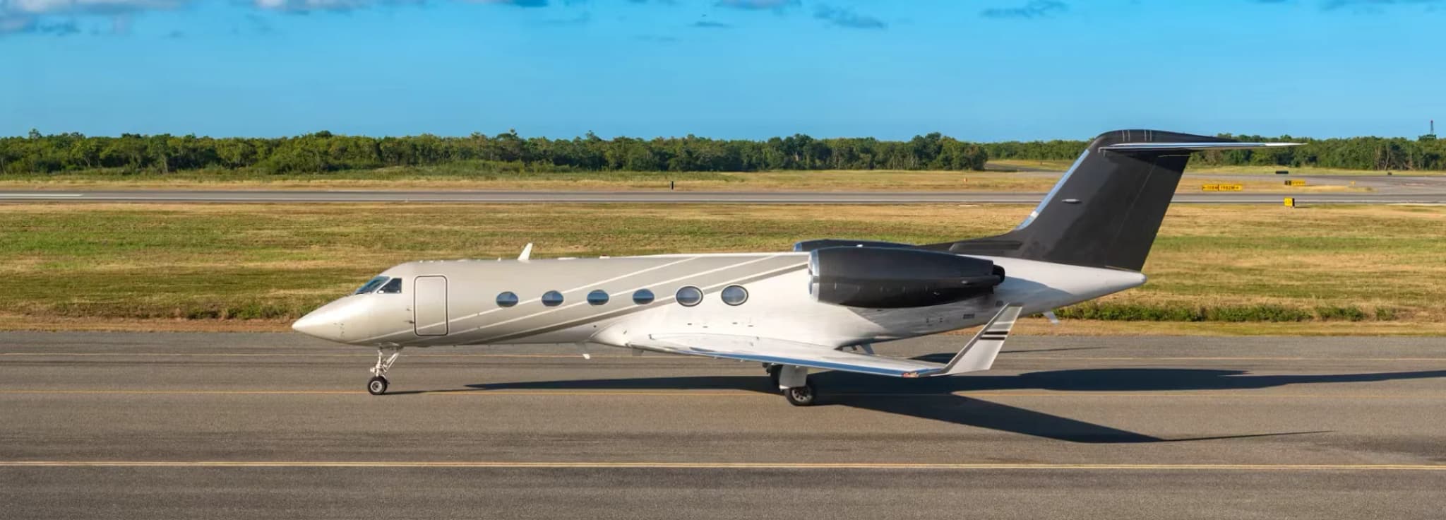 A luxury private business jet taxiing on an airport runway under a bright blue sky with white clouds.