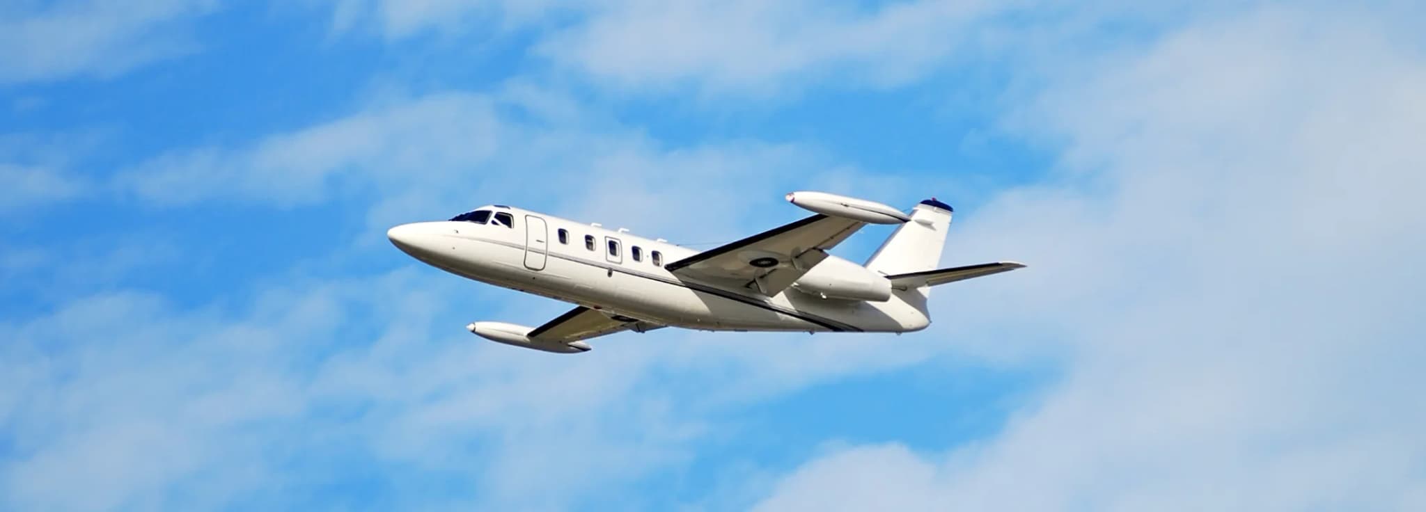A private jet aircraft in flight against a bright cloudy blue sky during a charter trip.