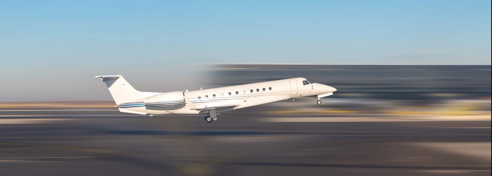 A white private jet aircraft captured with motion blur taking off from an airport runway against a clear blue sky