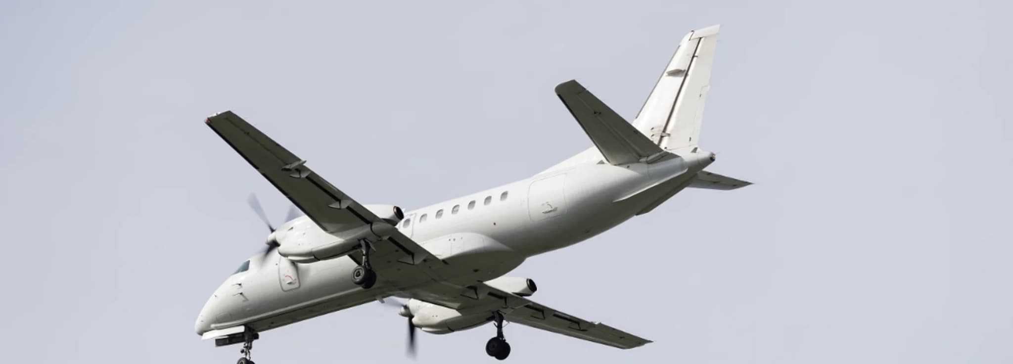 Saab 340B twin-engine regional turboprop aircraft landing with gear extended against a clear sky.