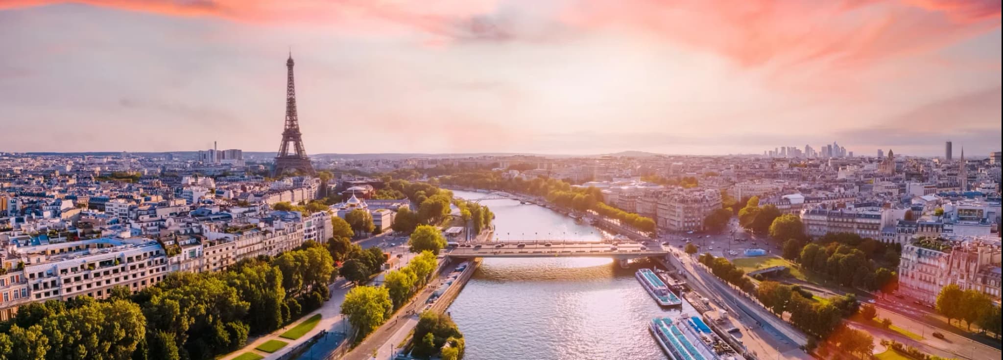 Panoramic sunset view over Paris, featuring the Eiffel Tower, the River Thames/Seine, and boats under a vibrant pink and orange sky.
