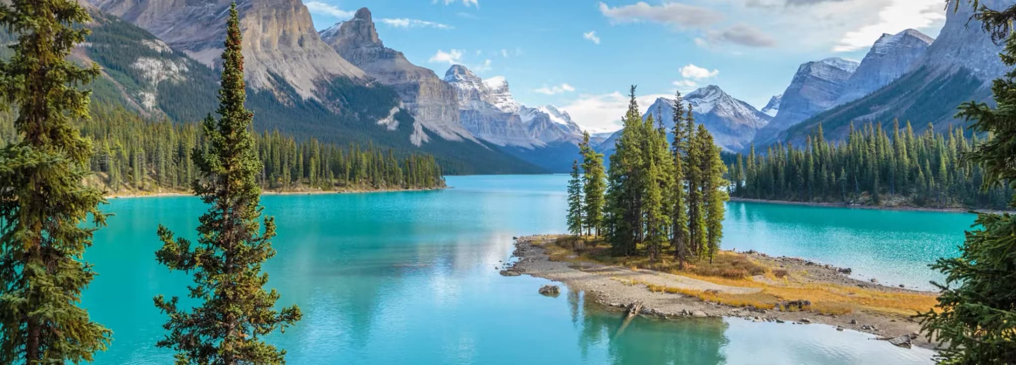 Classic view of Spirit Island on Maligne Lake in Jasper National Park, framed by evergreen trees with towering snow-capped mountains.