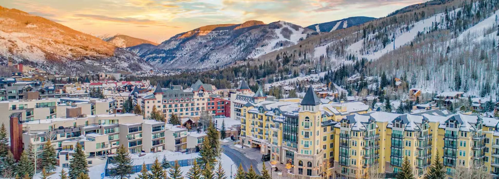 Aerial drone view of snow-covered luxury resort lodges in Lionshead Village Vail at sunset with ski slopes in the background