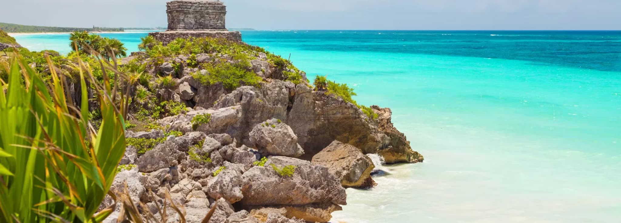 Ancient Maya stone temple perched on a rocky cliff overlooking turquoise Caribbean waters in Tulum, Mexico.