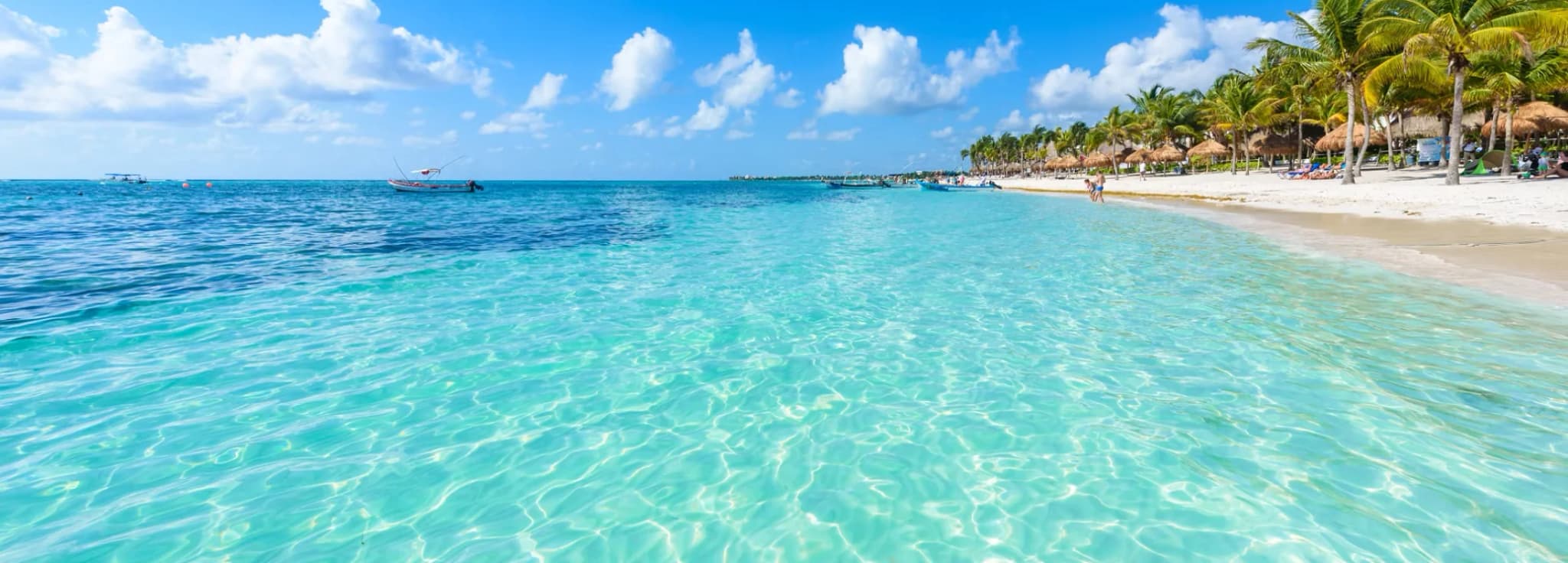Pristine tropical white sand beach lined with palm trees and clear shallow turquoise water in Cancun, Mexico.
